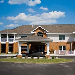 A large residential building with a brick facade, featuring multiple windows and a covered entrance, set against a partly cloudy sky.