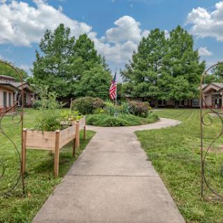 A peaceful pathway leading through a garden area with lush greenery and an American flag.