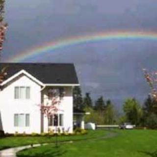 A beautiful rainbow arches over a house in a serene landscape.