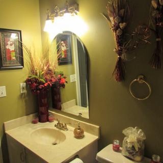 A warmly lit bathroom with decorative flowers, a mirror, and green walls.
