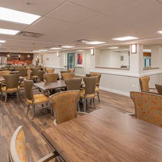 An empty dining area with wooden flooring, tables, and chairs arranged neatly under ceiling lights.