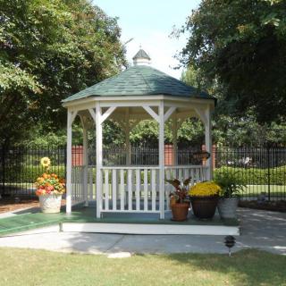 A charming gazebo surrounded by a garden with various potted flowers and trees.