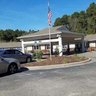 A building with a parking lot and an American flag in front, surrounded by trees.