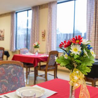 A cozy dining area set up with tables adorned with red tablecloths and decorative flower arrangements, showcasing a welcoming atmosphere.