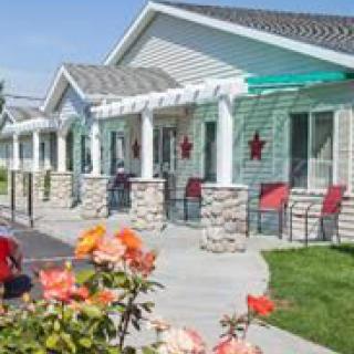 A row of residential buildings with front porches, chairs, and a garden with flowers on a sunny day.
