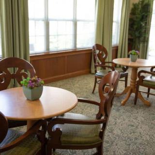 A cozy dining area with wooden tables and chairs, set beside large windows with green curtains.