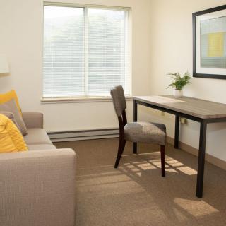 A minimalist office space with a desk, chair, sofa, and natural light from a large window.