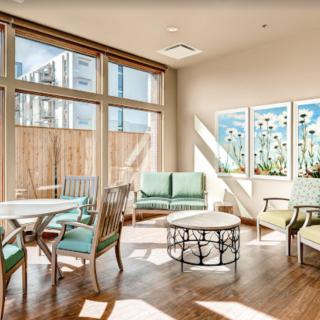 A well-lit modern living room featuring large windows, comfortable seating, and decorative artwork on the walls.