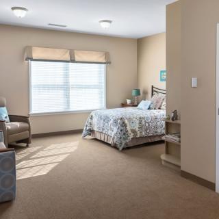 A cozy bedroom with a bed, chair, and window letting in natural light.
