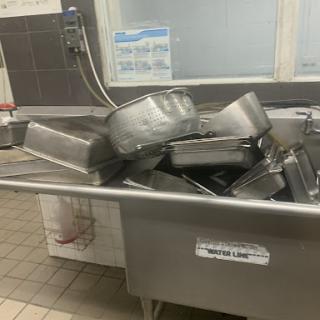 A stack of stainless steel serving trays piled in a commercial kitchen.