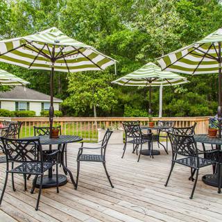 A scenic outdoor patio with tables and chairs under large umbrellas, surrounded by lush greenery.