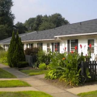 A row of white residential houses with manicured gardens and a walkway under a clear sky.