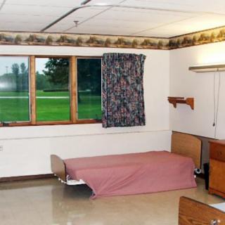 An empty hospital room with a single bed and a window with floral curtains.