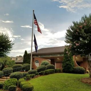 A building with flags surrounded by trees and a cloudy sky.