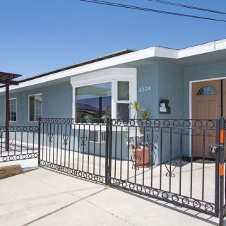 A single-story house with a modern design and a metal fence in front, under a clear blue sky.