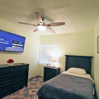 A cozy bedroom featuring a single bed, wall-mounted TV, and dresser.
