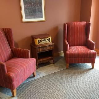 A cozy lounge area with two red striped chairs, a vintage radio on a small wooden table, and a painting hanging on the wall.