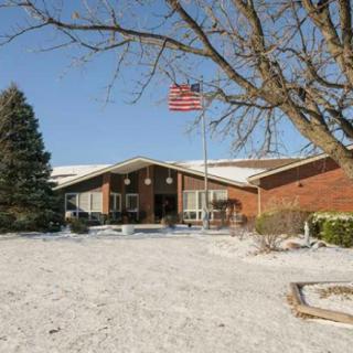 A snow-covered landscape showcasing a brick house with an American flag under a clear blue sky.