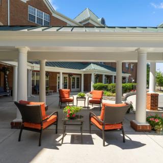 An outdoor patio area with comfortable seating, surrounded by garden and architectural columns.