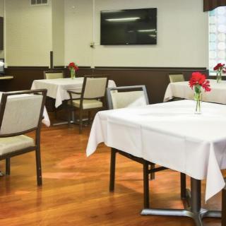An empty dining area with tables and chairs, adorned with tablecloths and flower arrangements.