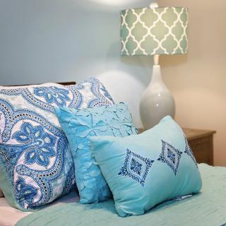 A cozy bedroom setup featuring blue-themed decorative pillows and a stylish table lamp.