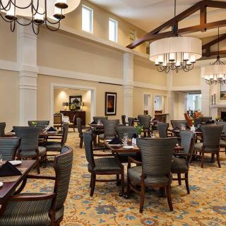 A spacious and elegantly decorated dining room with multiple tables and chairs, large chandeliers, and patterned carpet.