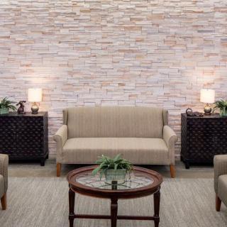 A cozy living room with a beige sofa, armchairs, a round wooden coffee table, and decorative lamps against a brick wall.