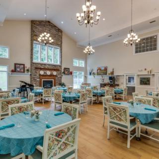 A spacious and elegant dining room with teal-covered tables, decorative chairs, chandeliers, a fireplace, and large windows.