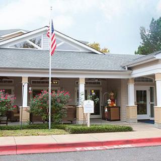 The image shows the entrance of a building with an American flag, surrounded by trees and shrubs.