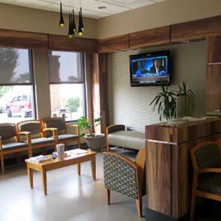 A modern waiting room with chairs, a television, and decorative plants.
