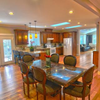 A modern open floor plan kitchen and dining area with elegant lighting and wood flooring.