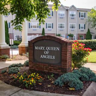 Entrance sign of Mary, Queen of Angels facility surrounded by landscaped gardens and flowers.