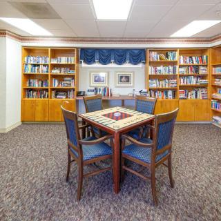 A cozy library reading area with bookshelves and a central table surrounded by chairs.