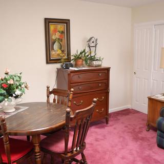 A cozy living space featuring a dining table with chairs, a wooden dresser, and plush carpeting.