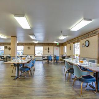 A spacious dining hall with neatly arranged tables and chairs, featuring ample lighting and large windows.