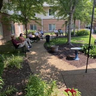 A serene garden setting with people relaxing on benches along a tree-lined pathway.