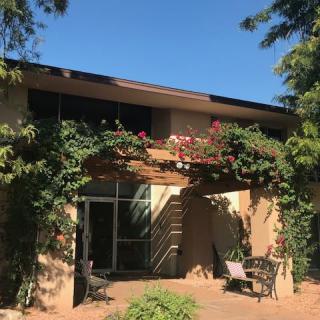 A cozy house with a vine-covered pergola and outdoor seating on a sunny day.