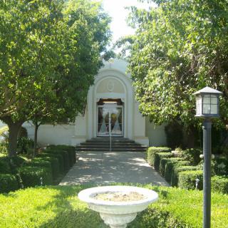 A picturesque garden pathway leading to a building entrance, surrounded by lush greenery and trees.