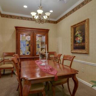 A cozy dining room with a wooden table, chairs, and a glass-front cabinet, adorned by a chandelier and wall art.