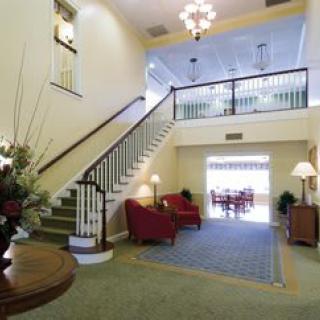 A well-lit lobby featuring a grand staircase, comfortable armchairs, and elegant decor.