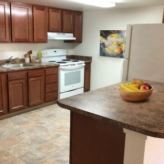 A kitchen with wooden cabinets, a stove, refrigerator, and a countertop featuring a fruit bowl.