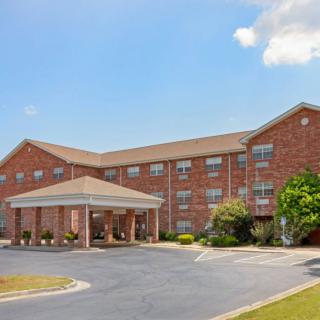 A three-story brick hotel building with a covered entrance and an adjacent parking lot under a clear blue sky.