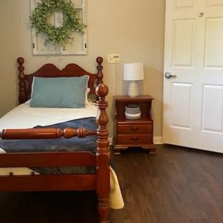 A cozy bedroom with a wooden bed and nightstand, complemented by a lamp and wall wreath.