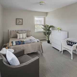 A minimalist bedroom with neutral colors, featuring a bed, a chair, and a dresser.