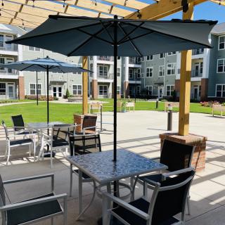 A sunny courtyard with outdoor seating and umbrellas at an apartment complex.