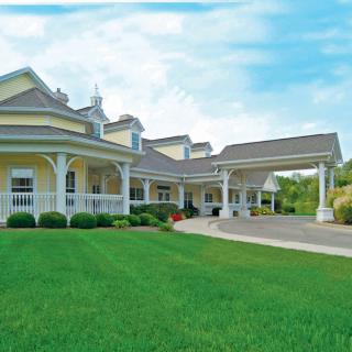 A large yellow residential building with a porch and well-maintained lawn under a blue sky.