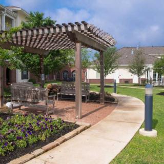A beautifully landscaped garden features a pergola with outdoor seating along a curved walkway.