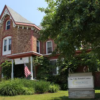 A historic brick house with an American flag and lush greenery on a sunny day.