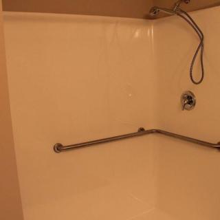 A bathroom shower with a handheld showerhead and grab bar.