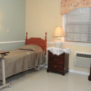 A simple hospital room with a single bed, a side table, and a lamp by the window.
